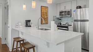 A modern kitchen with white cabinetry, stainless steel appliances, pendant lighting, and a central island with stools. - Elation 2BR: Sunset Views & Steps to Baytowne (Miramar Beach)