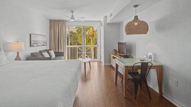 A hotel room with a bed, a desk with a chair, a ceiling fan, and a large window with curtains. - Elation 2BR: Sunset Views & Steps to Baytowne (Miramar Beach)