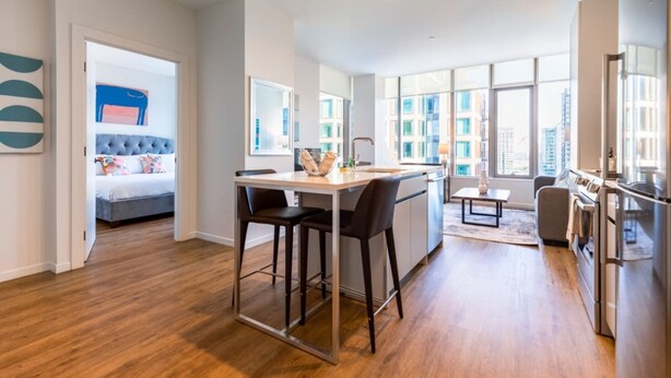 A modern apartment with a dining area, kitchen, and a bedroom with a large window. - Seaport Apt with City Views and Pool (Boston)
