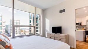 A modern bedroom with a large bed, a TV on a dresser, and a view of the city through large windows. - Seaport Apt with City Views and Pool (Boston)