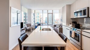 A modern kitchen with a central island, built-in appliances, and large windows offering city views. - Seaport Apt with City Views and Pool (Boston)