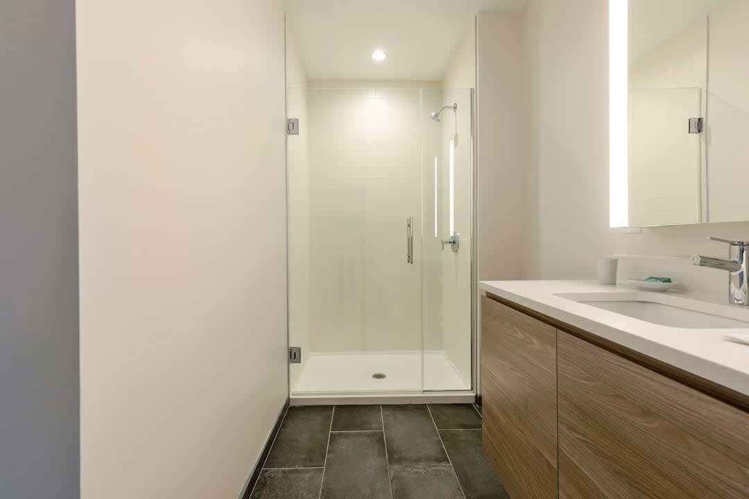 Ein modernes Badezimmer mit einer begehbaren Glasdusche, einem Holzwaschtisch und einem gro ßen Spiegel.