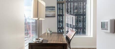 A modern office space with a wooden desk, a lamp, a chair, and a view of a cityscape through large windows.