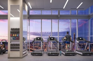 A gym with treadmills, a weight rack, and a city view through large windows.
