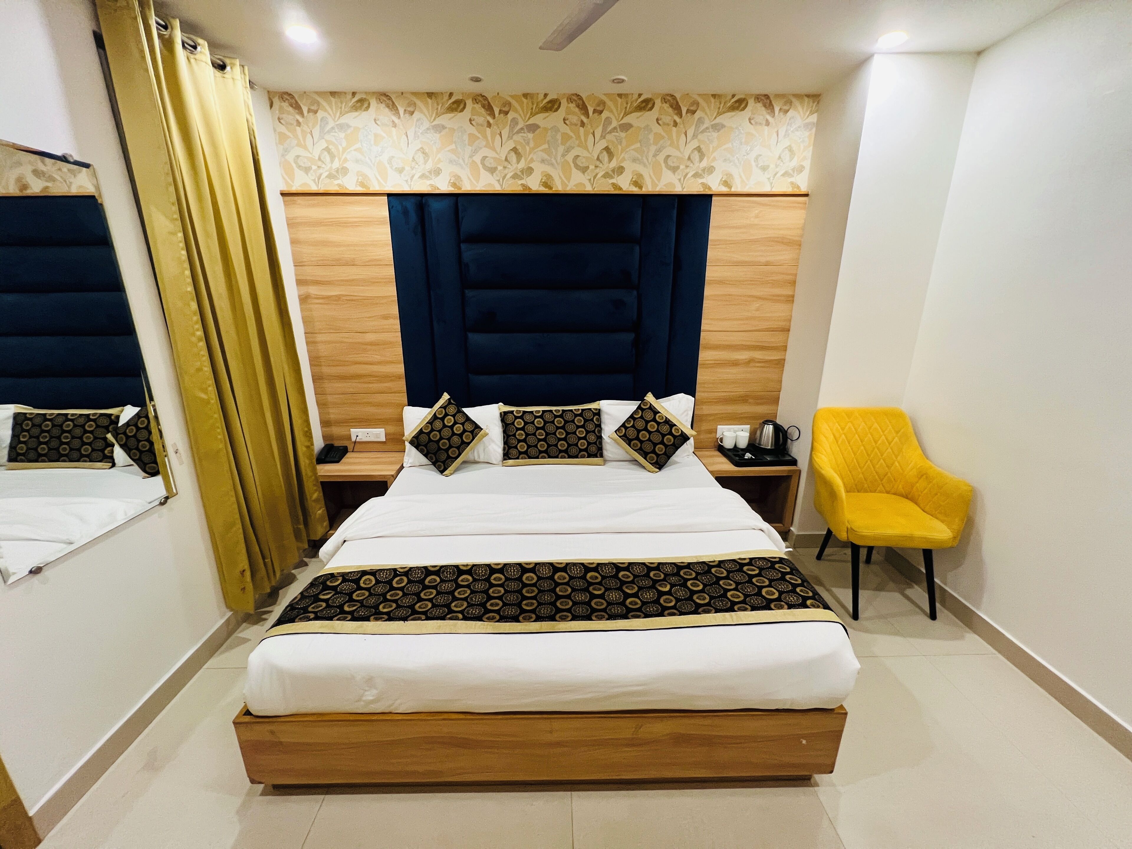 A modern hotel room with a large bed, wooden headboard, and a yellow armchair.