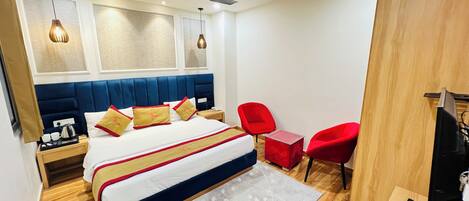 Una habitación de hotel moderna con una cama grande, dos sillas rojas, un escritorio de madera y un ventilador de techo.
