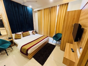 A hotel room with a large bed, two chairs, a desk with a TV, and a window with curtains.