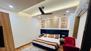 Une chambre d’hôtel moderne avec un grand lit, un fauteuil rouge, un ventilateur de plafond et un appareil de climatisation.