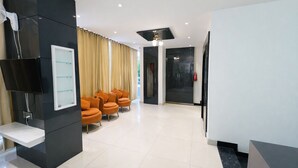 Un espace d’accueil moderne doté d’un téléviseur à écran plat, d’un tableau blanc et d’une rangée de chaises orange.