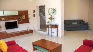 A living room with a TV, wooden shelves, a red sofa, a grey sofa, and a wooden coffee table. - Green Relax Arenella (Arenella)