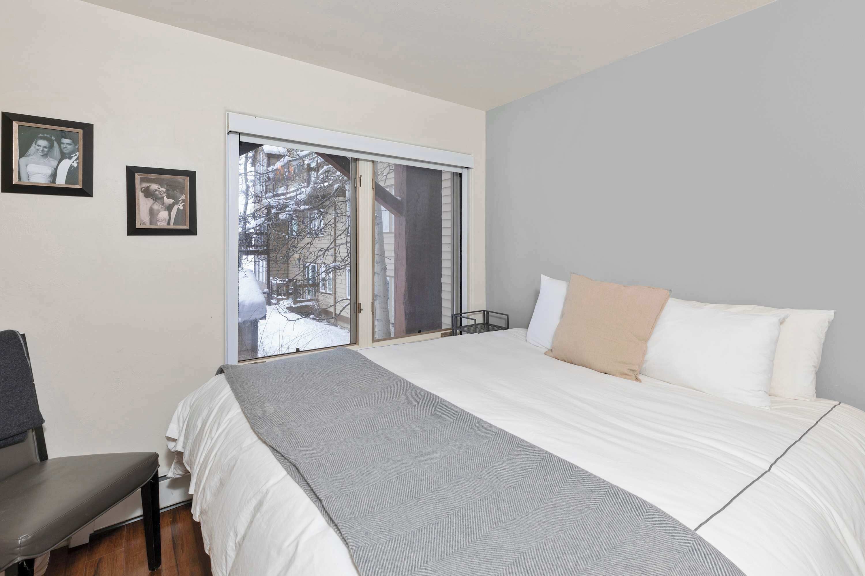 A bedroom with a bed, a chair, a window with a view of a snowy street, and two framed photos on the wall.