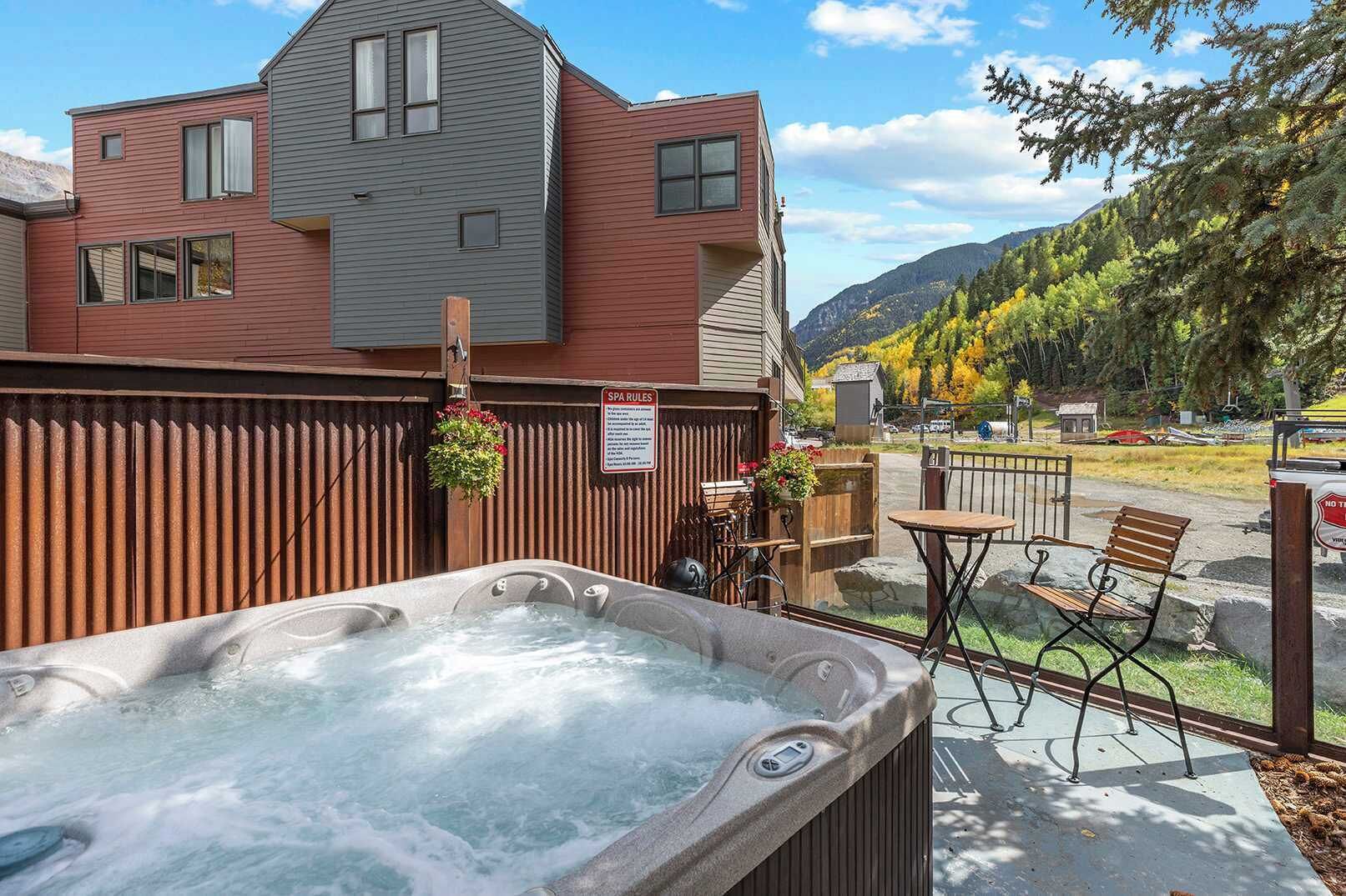 A hot tub with a wooden fence, a sign with spa rules, and a mountain view.