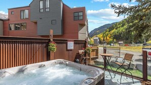 Un bain à remous entouré d’une clôture en bois, un panneau indiquant les règles du spa et une vue sur la montagne.