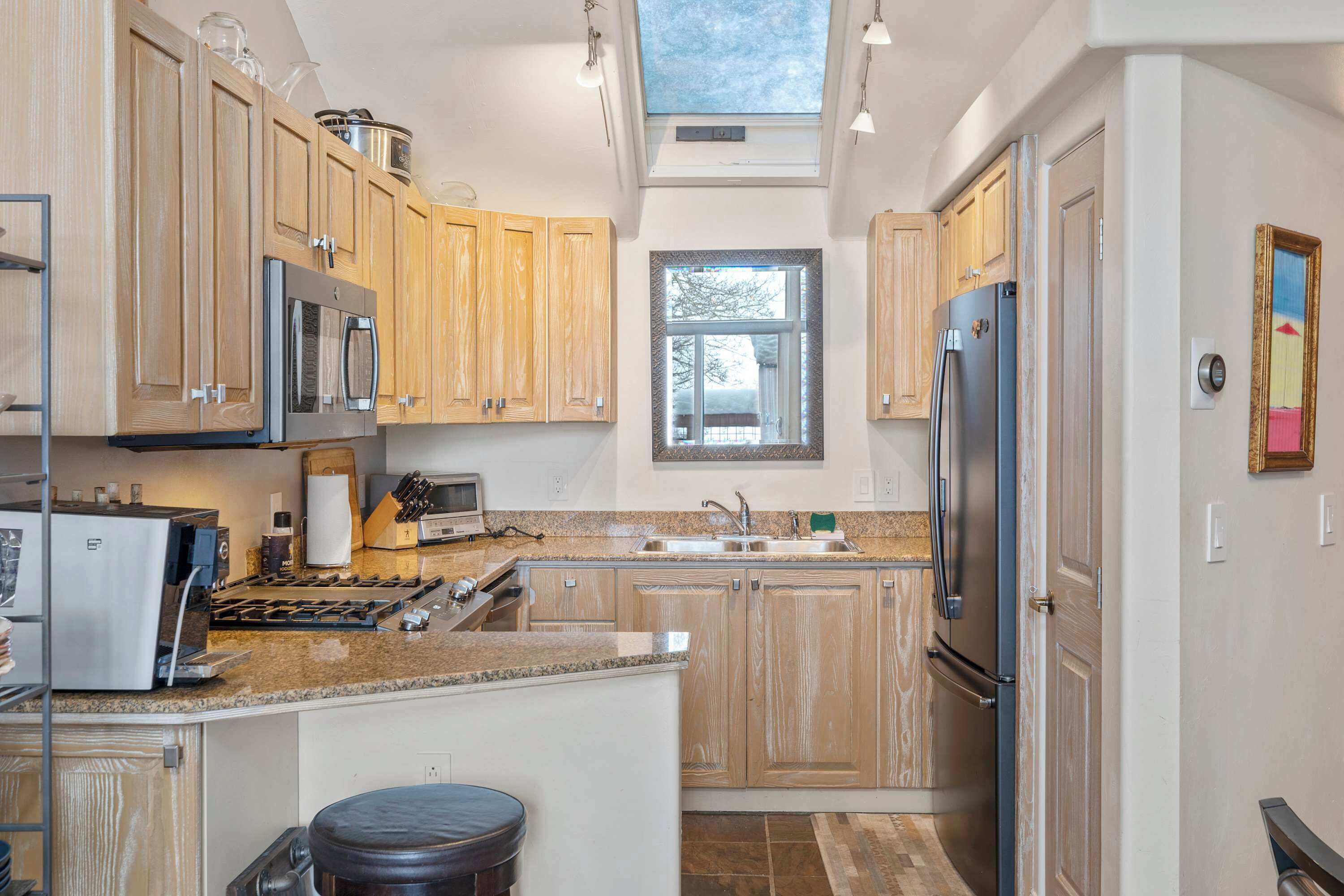 A kitchen with wooden cabinets, stainless steel appliances, a granite countertop, and a skylight.