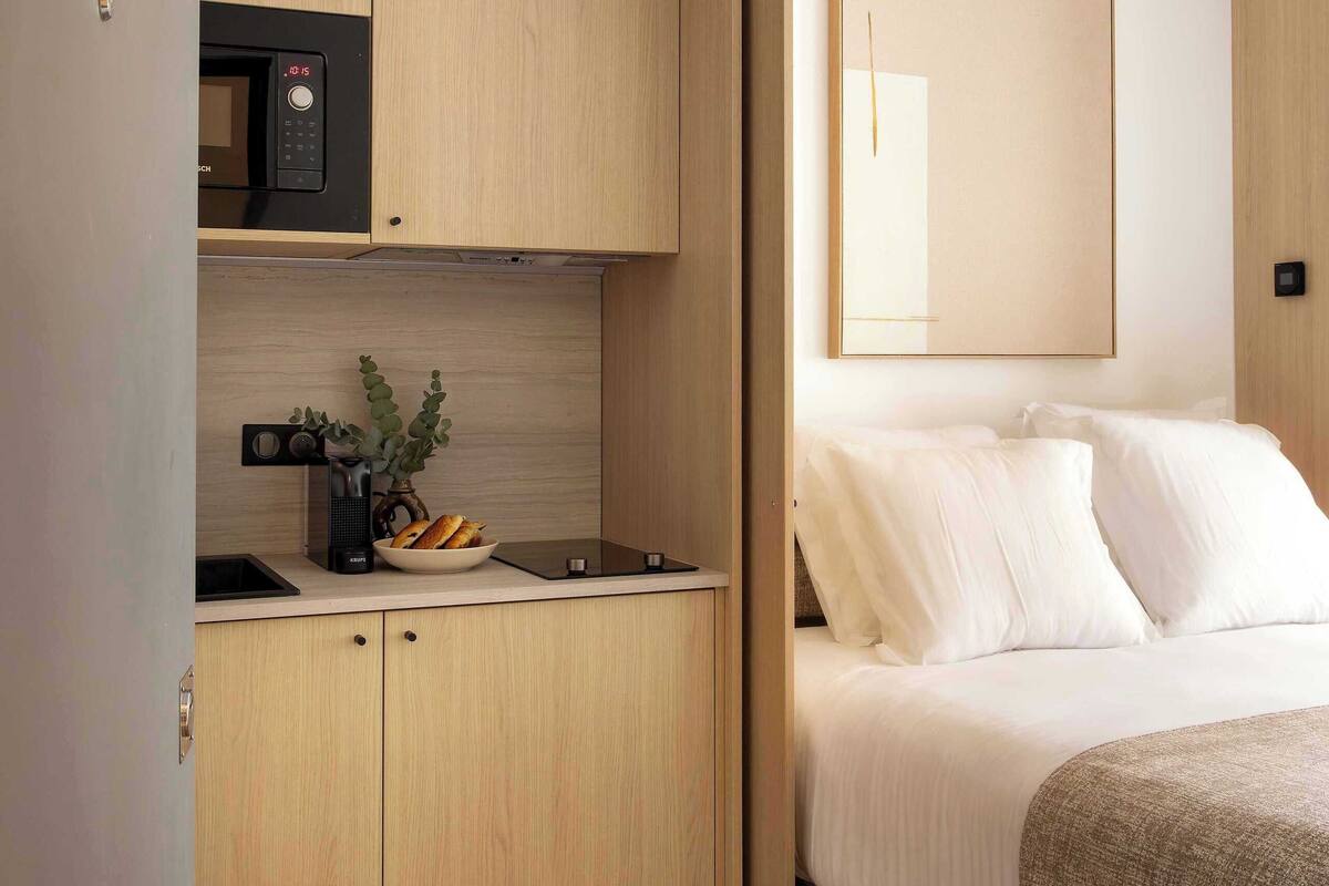 A compact room with a kitchenette, a bed, and a large mirror.