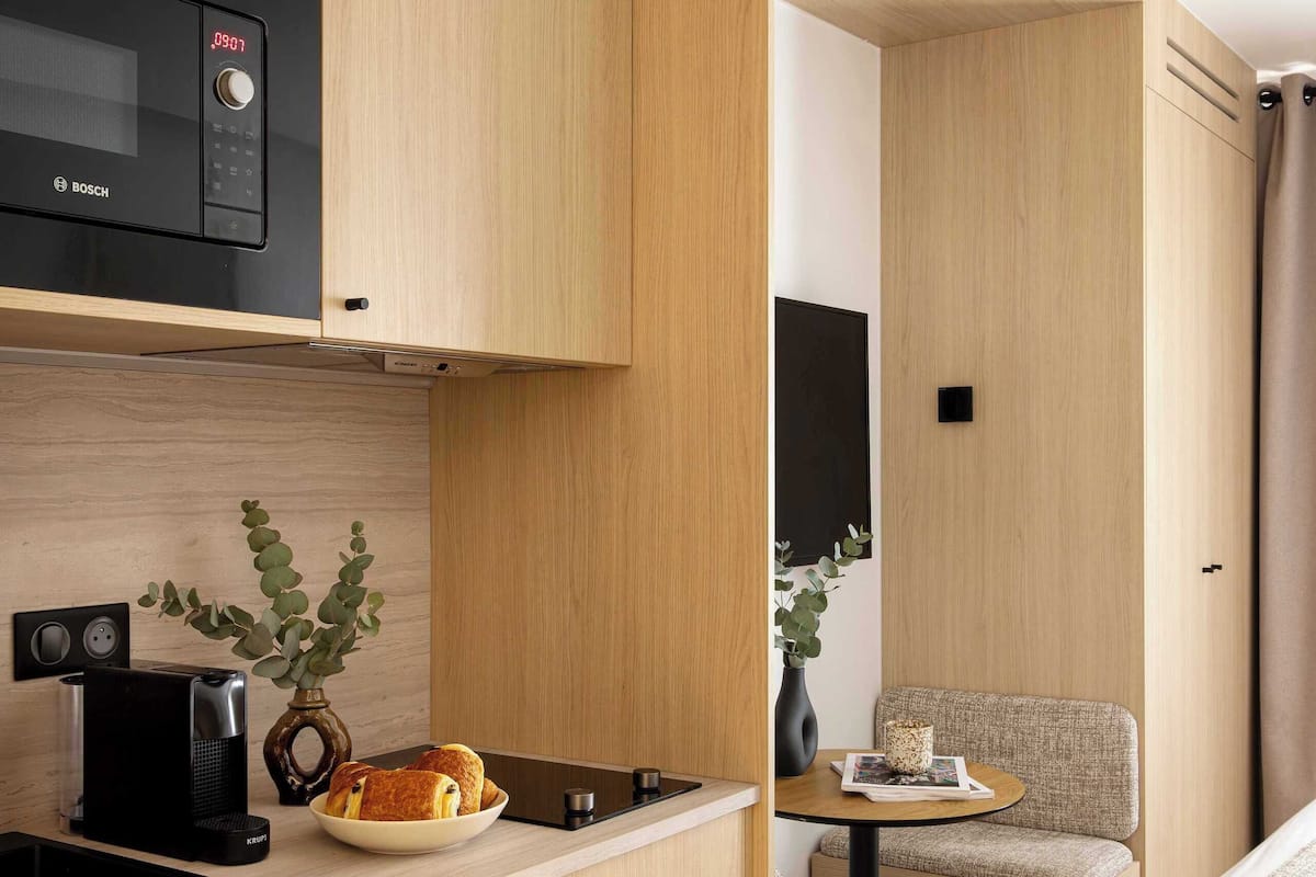 A compact kitchenette with a Bosch microwave, a coffee maker, and a vase with greenery. There is a small dining area with a table and a chair.