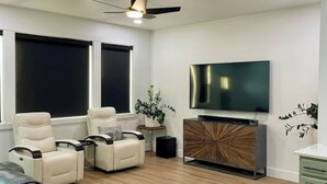 Un salon moderne doté d’un téléviseur à écran plat, de canapés en cuir, d’un ventilateur de plafond et d’un meuble en bois.