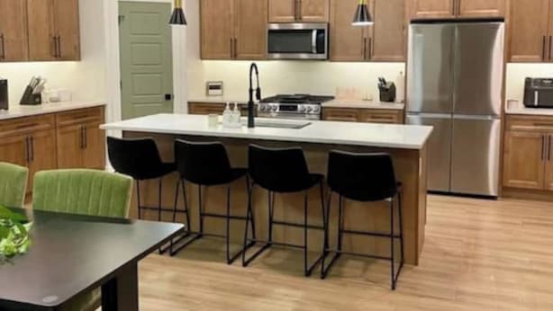 Une cuisine moderne avec des meubles en bois, un réfrigérateur en acier inoxydable, un four à micro-ondes et un îlot central doté de tabourets de bar.