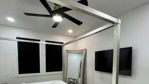 Une chambre à coucher avec un lit, un ventilateur de plafond, une télévision et une fenêtre.