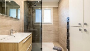 Un bagno moderno con cabina doccia in vetro, mobile lavabo in legno e uno specchio grande.