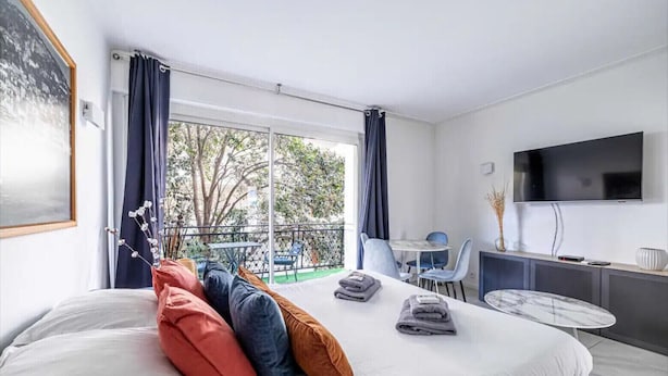Camera d'albergo con un letto, una scrivania, una sedia, una TV e un balcone con vista sugli alberi.