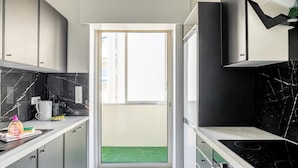 Una cucina moderna con schienale in marmo nero, elettrodomestici in acciaio inossidabile e vista su una zona esterna verde attraverso una porta in vetro.
