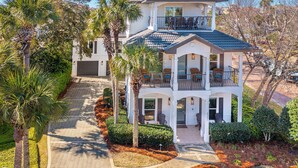 A two-story house with a balcony, a covered patio, and a driveway. - Beautiful Home & Carriage House with Golf Cart (Destin)