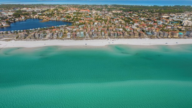 An aerial view of a coastal town with a beach, clear turquoise waters, and a mix of residential and commercial buildings. - Beautiful Home & Carriage House with Golf Cart (Destin)
