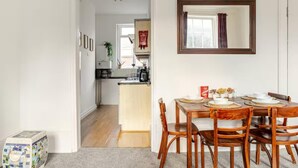 Ein Essbereich mit Holztisch und Stühlen, im Hintergrund eine Küche und ein Spiegel an der Wand.