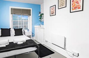 A room with a bed, a window with blinds, a small desk with a plant, and three framed pictures on the wall. - Camden 3-bed, Sleeps 6, 1 Min to Tube & Parking (London)