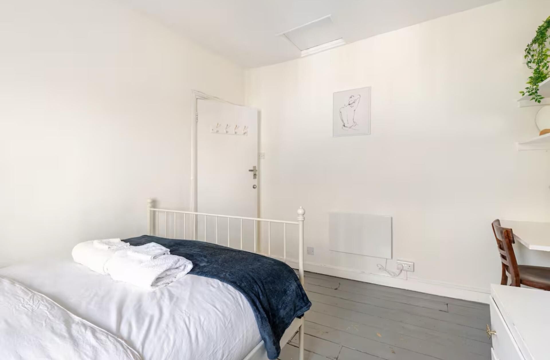 A bedroom with a bed, a door, a wall-mounted radiator, and a small desk with a chair.