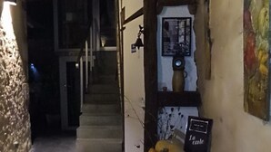 A narrow stone corridor with a staircase leading to an upper level. A small table with a book and a vase is placed against the wall.