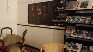 A dining area with a round table, two chairs, a poster on the wall, and a bookshelf with brochures.