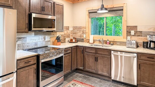 Une cuisine moderne avec des meubles en bois, des appareils électroménagers en acier inoxydable, une fenêtre donnant sur la verdure et un four encastré.