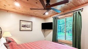 A bedroom with a bed, a ceiling fan, a TV mounted on the wall, a window with curtains, and a framed picture on the wall. - Ronnie's Guest House (Inlet)