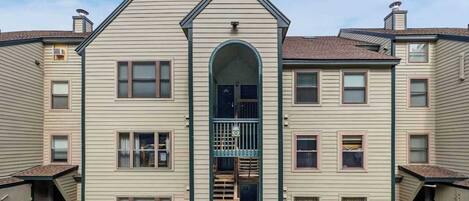 A multi-story residential building with a central entrance, multiple windows, and a small porch area.