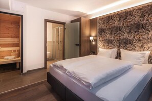 Una habitación de hotel con una cama, un banco de madera, ducha y pared con estampado.