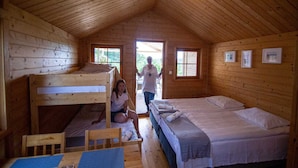 Una baita con interni in legno, letti a castello, un letto singolo e un tavolo con sottopiatti blu.