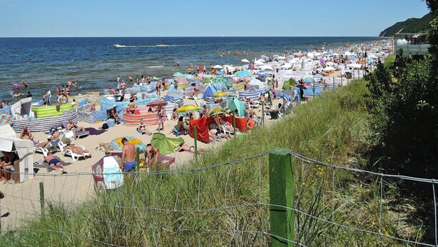 Una spiaggia affollata, piena di ombrelloni e bagnanti.