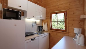 Una cucina compatta con mobili bianchi, un forno a microonde, una macchina per caffè e una finestra vista verde.