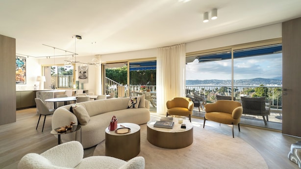 Un salon moderne avec une grande fenêtre, un canapé, deux fauteuils et une table basse.