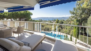 Un balcon avec des fauteuils de jardin et une vue sur une piscine et un paysage.