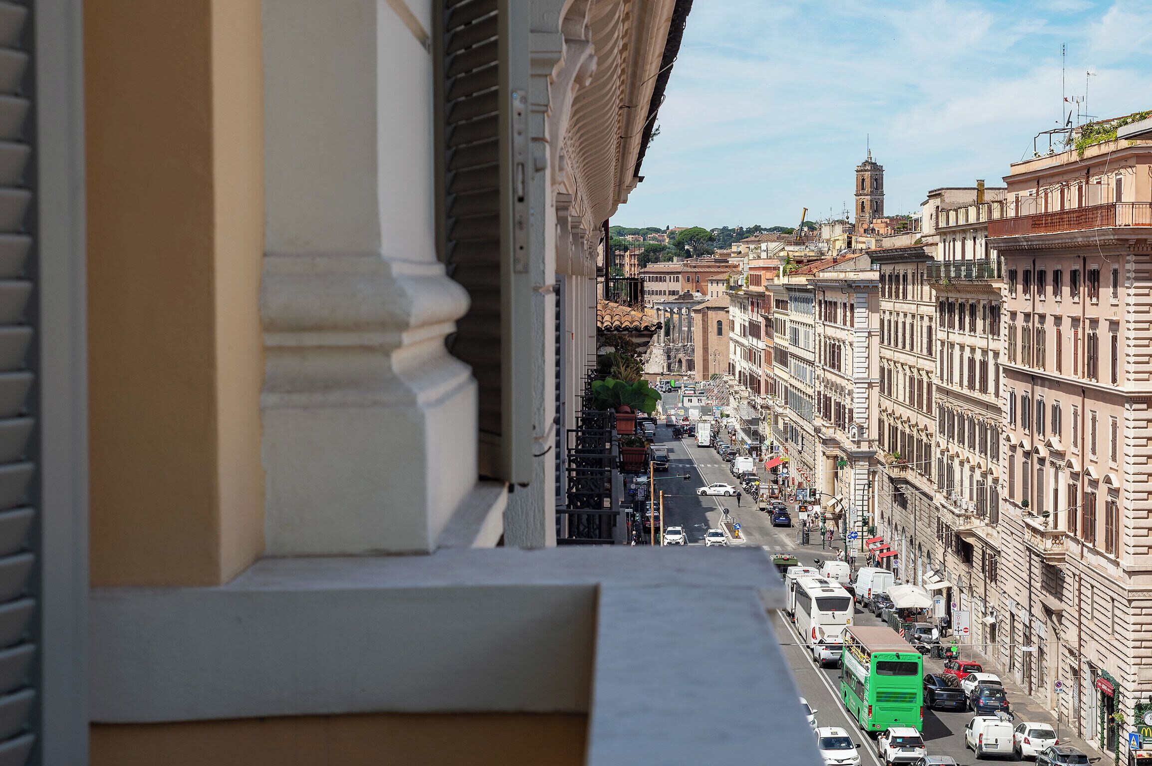Vista de una calle urbana desde un balcón, con edificios, vehículos y una torre a lo lejos.