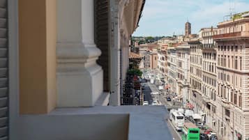 Vista de una calle urbana desde un balcón, con edificios, vehículos y una torre a lo lejos.