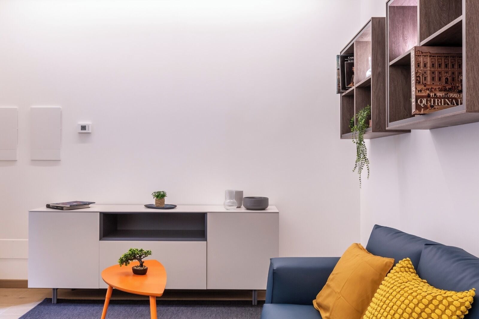 A modern living room with a sofa, a coffee table, a small orange table, and a white cabinet with shelves.
