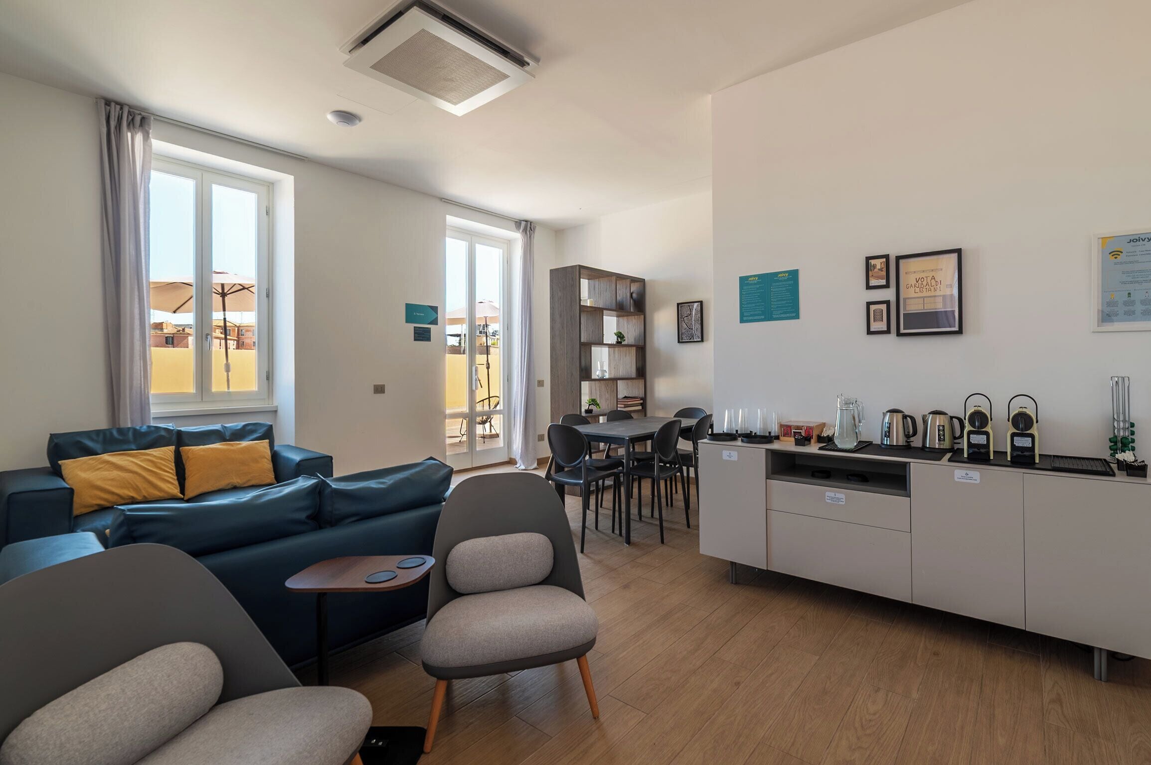 Una sala moderna con sofá, sillones, un comedor con mesa y sillas, y una cocina equipada.