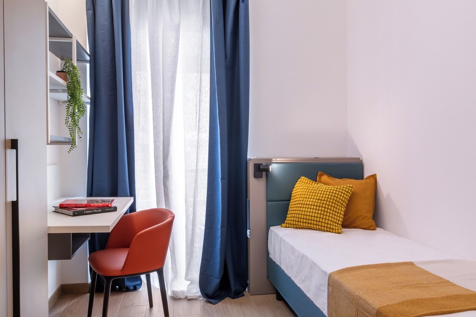 A bedroom with a bed, a desk, a chair, and a window with curtains.