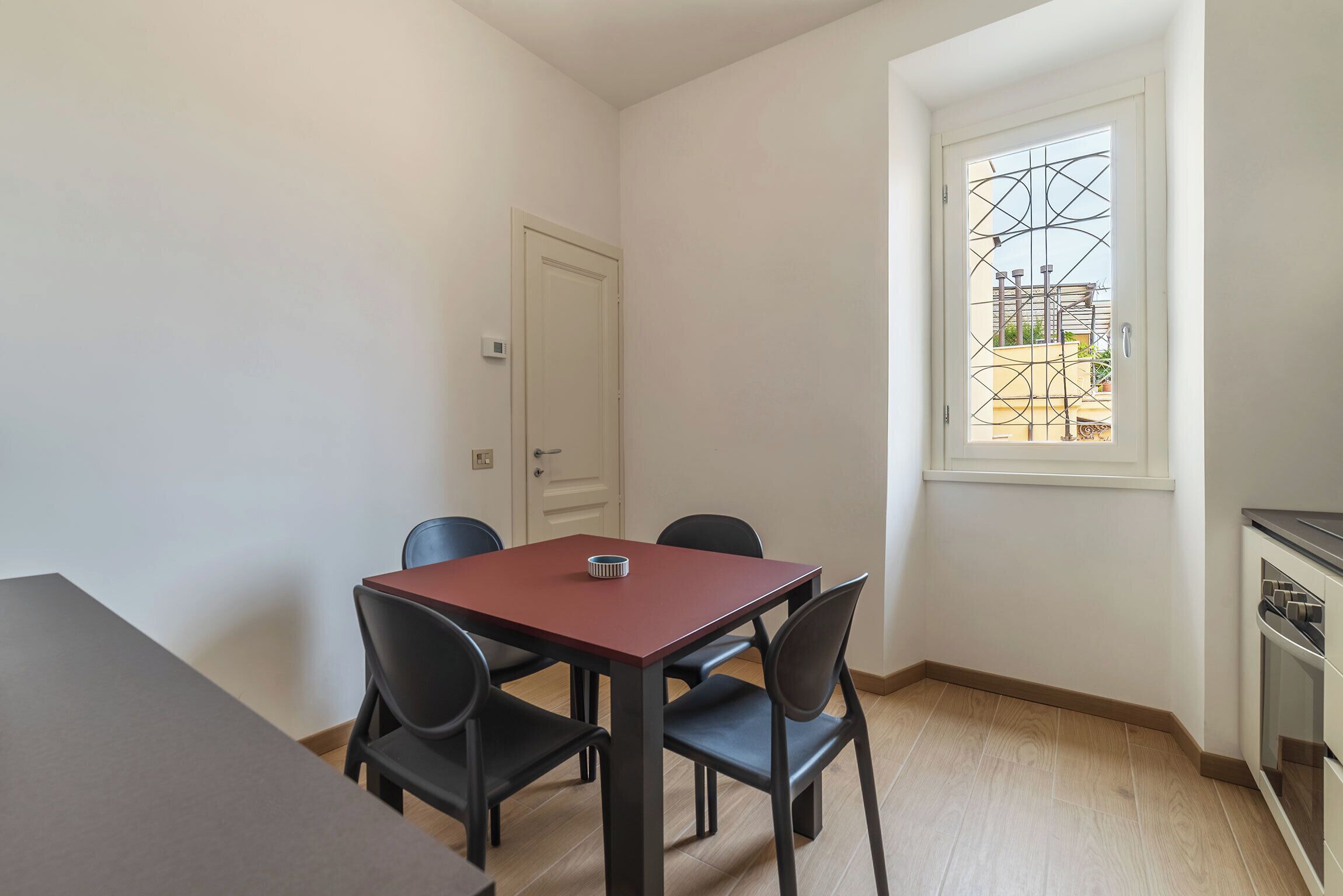 A small dining area with a table and four chairs, a white door, and a window with a metal gate.