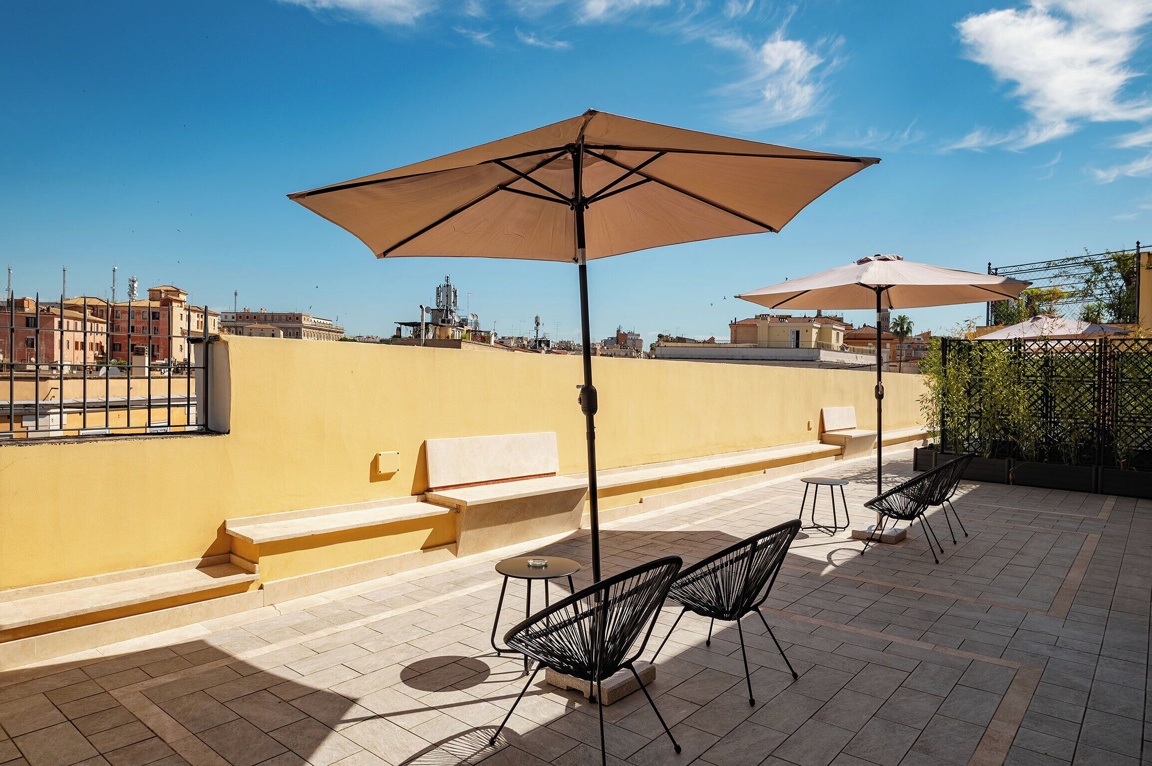 A rooftop terrace with outdoor seating, including a bench and chairs, and two large umbrellas providing shade.