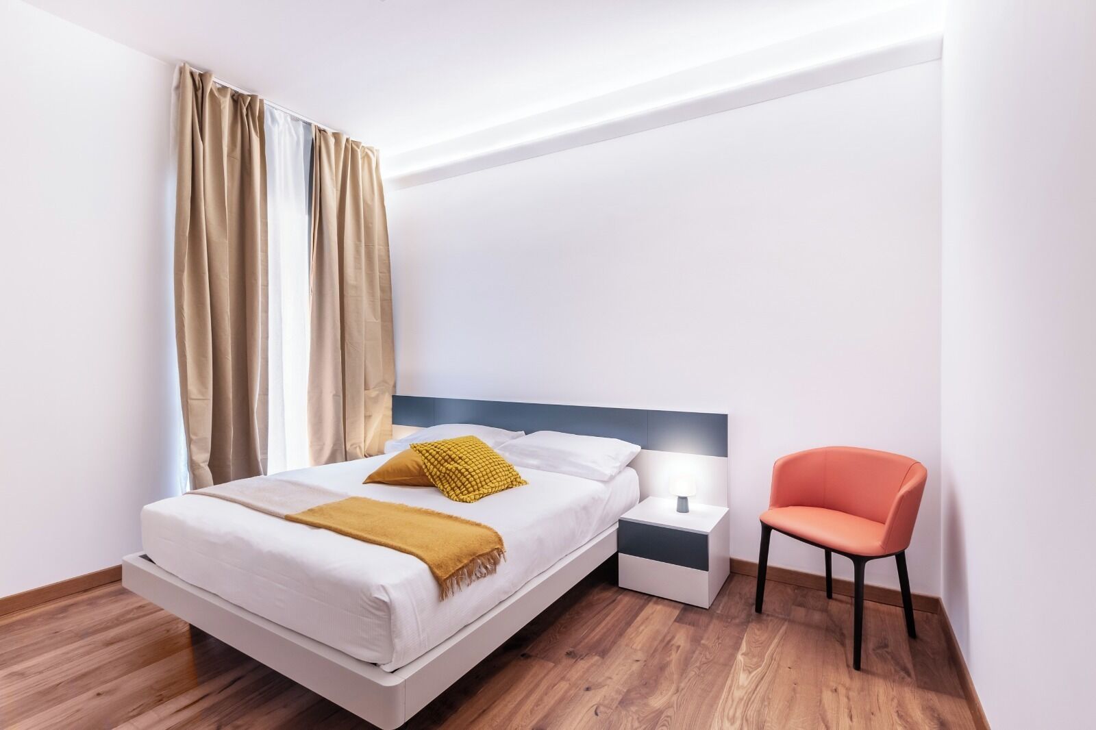 A modern hotel room with a bed, a nightstand, a lamp, and a chair.